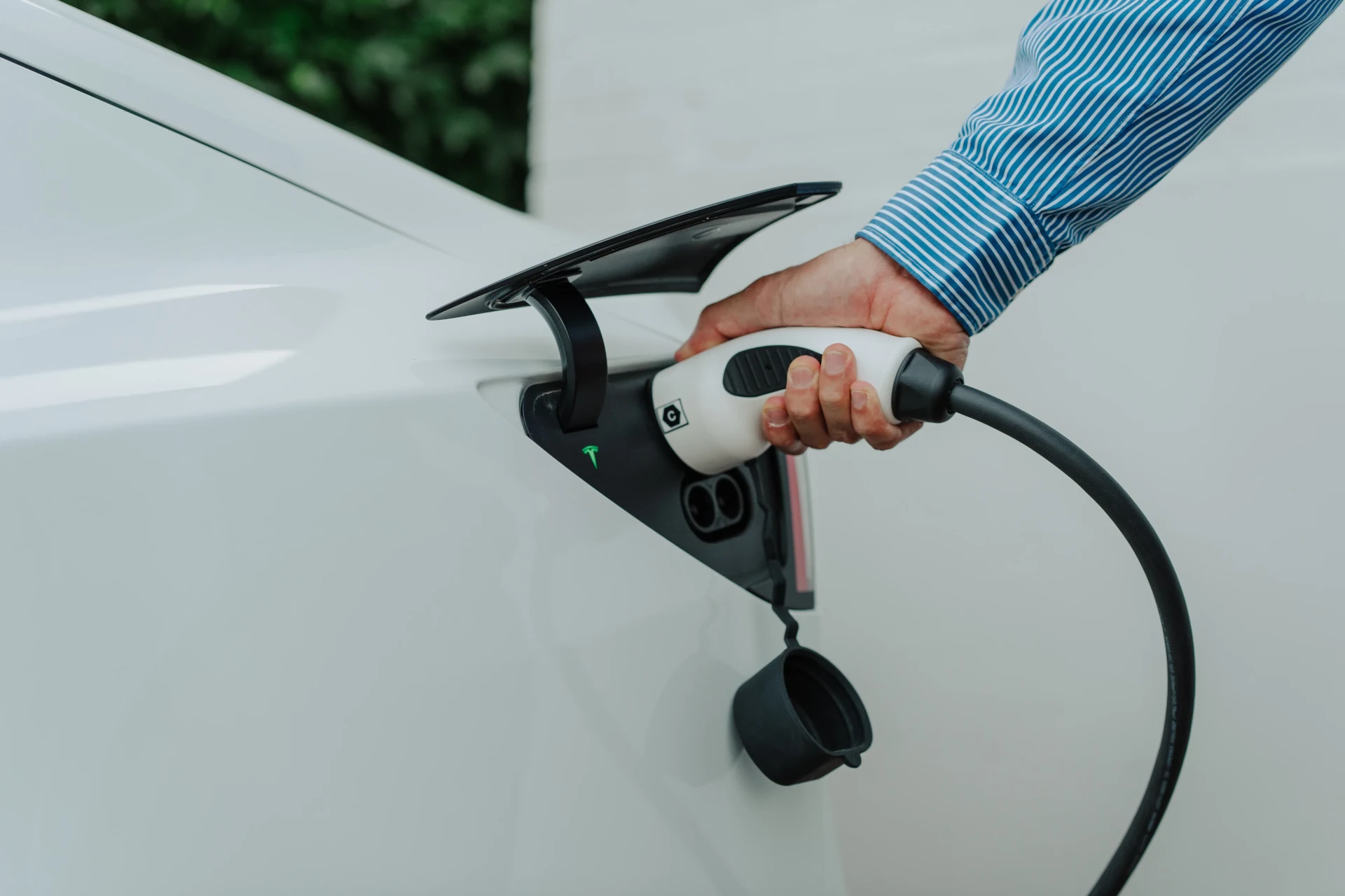 A person inserting an electric vehicle charging plug into an EV.