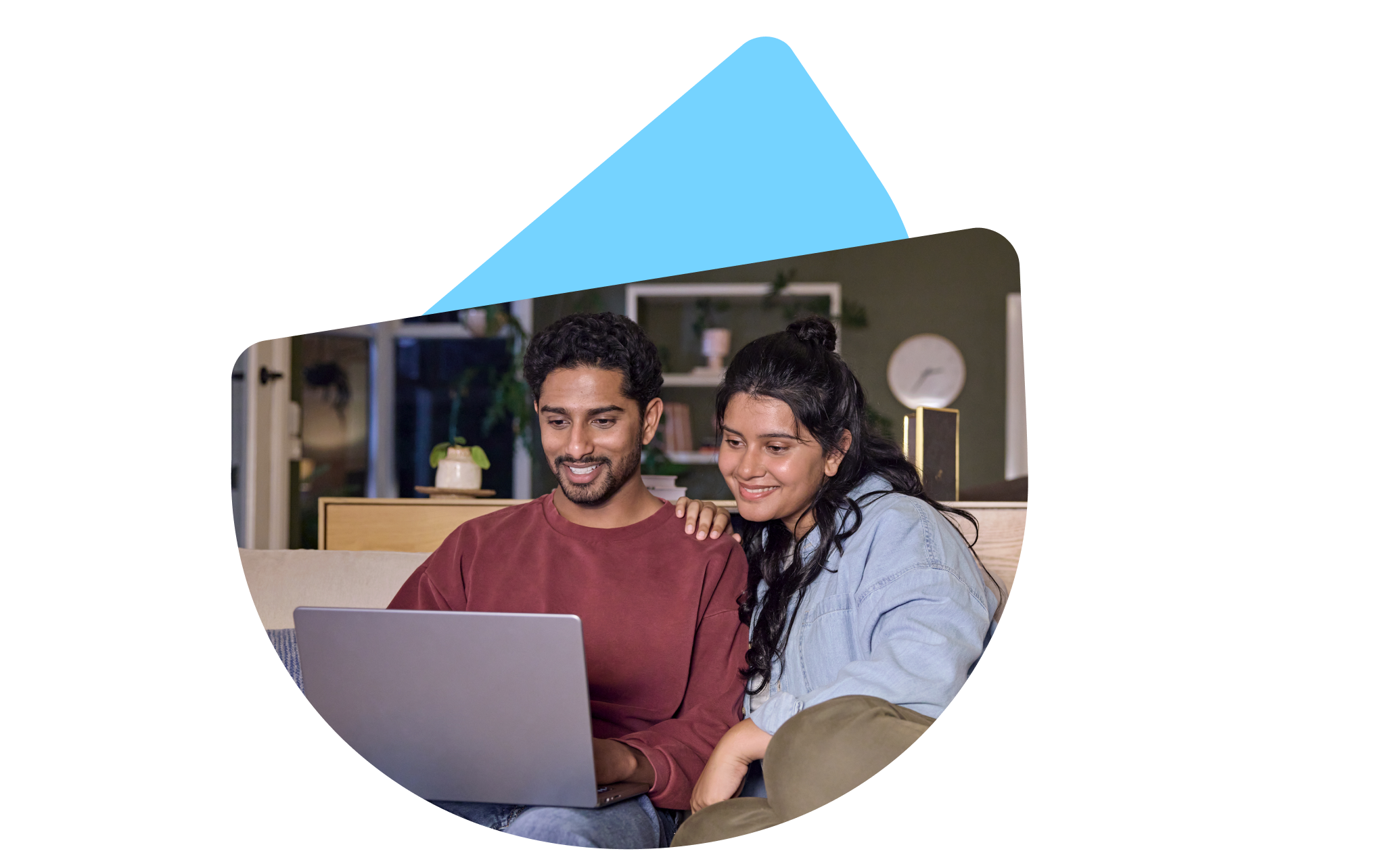 Two people seated together on a sofa, viewing a laptop in a home setting.