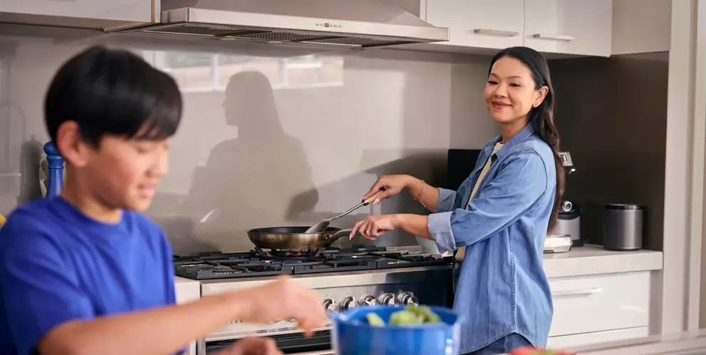 A person cooking at a stove while a child prepares food at the kitchen counter.