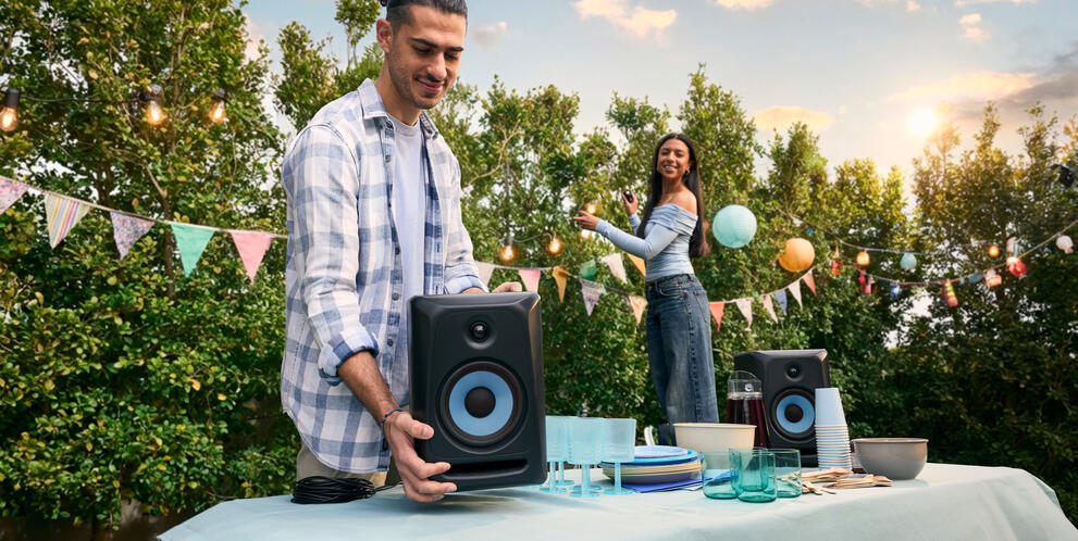 People setting up an outdoor party with speakers and decorations on a table in a backyard.