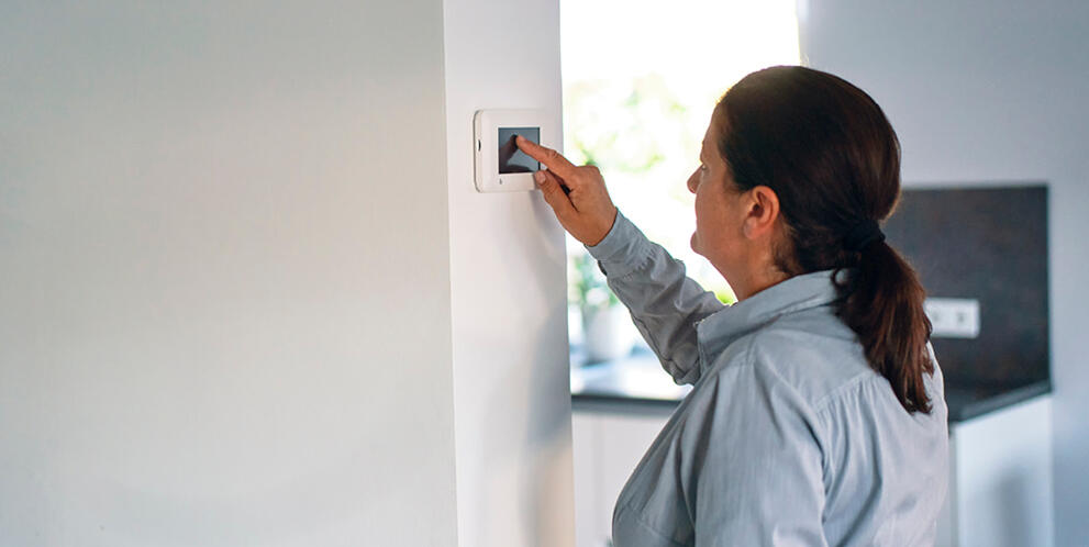 A person reaching out to adjust a wall-mounted digital thermostat inside a modern home.