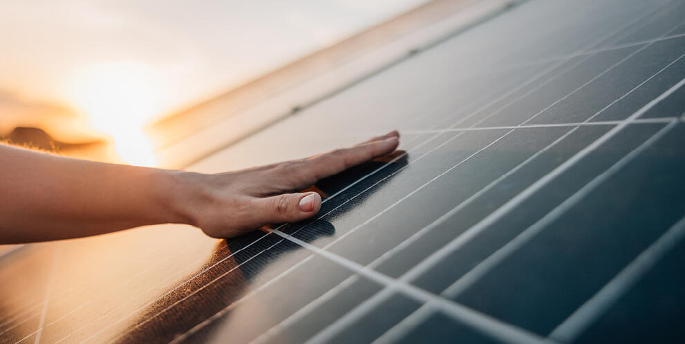Hand touching a solar panel surface during sunset
