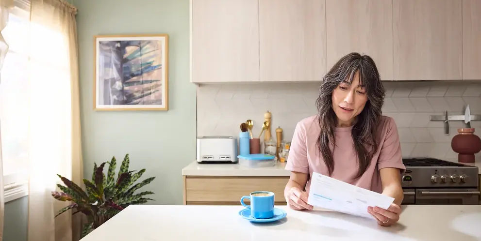 A woman reading her bill while sitting at the kitchen table.