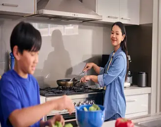 A person cooking at a stove while a child prepares food at the kitchen counter.