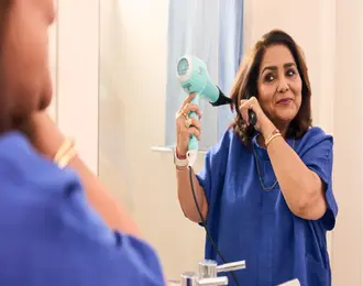 A person drying their hair with a hairdryer in front of a bathroom mirror.
