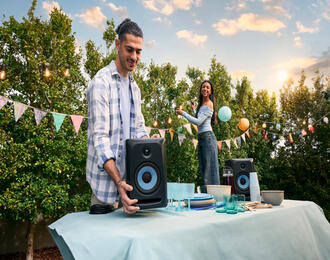 People setting up an outdoor party with speakers and decorations on a table in a backyard.