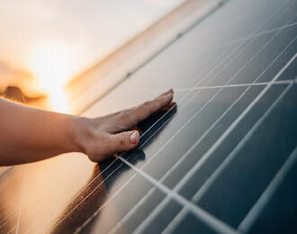 Hand touching a solar panel surface during sunset