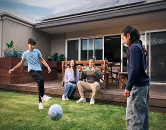 Two kids playing soccer in the backyard while their parents watch and take photos, enjoying family time at home.