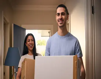 A smiling couple carrying moving boxes into a new home. ENGIE's moving home guarantee means their new home is already connected to energy.