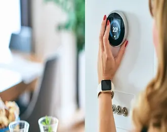 A woman adjusting an electronic thermostat at home.