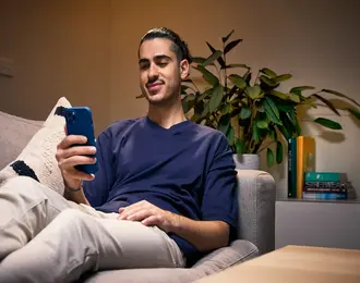A man using his smartphone while sitting on the living room couch.