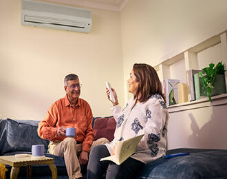 A couple sitting in the lounge room turning the air conditioner on.