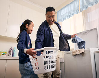 A father and daughter removing dry clothes from the washing machine.