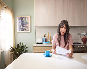 Person sits at a kitchen counter reading a bill with a cup of coffee nearby